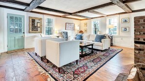 A room with exposed wooden beams, a white sofa, a striped bench, and a patterned rug. - Hillside Farmhouse, Updated & Pet-Friendly (Hartford)