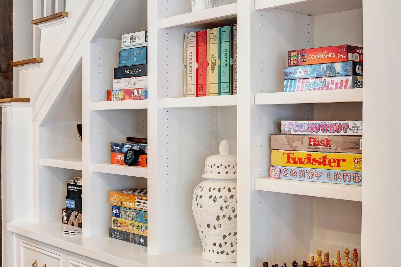 Ein Bücherregal mit verschiedenen Gesellschaftsspielen und Puzzles, einer Zierdevas und einer Treppe.