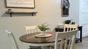 A dining area with a round table, white chairs, a potted plant, and a framed quote on the wall. - Cozy 2BR Lincoln House (Enid)