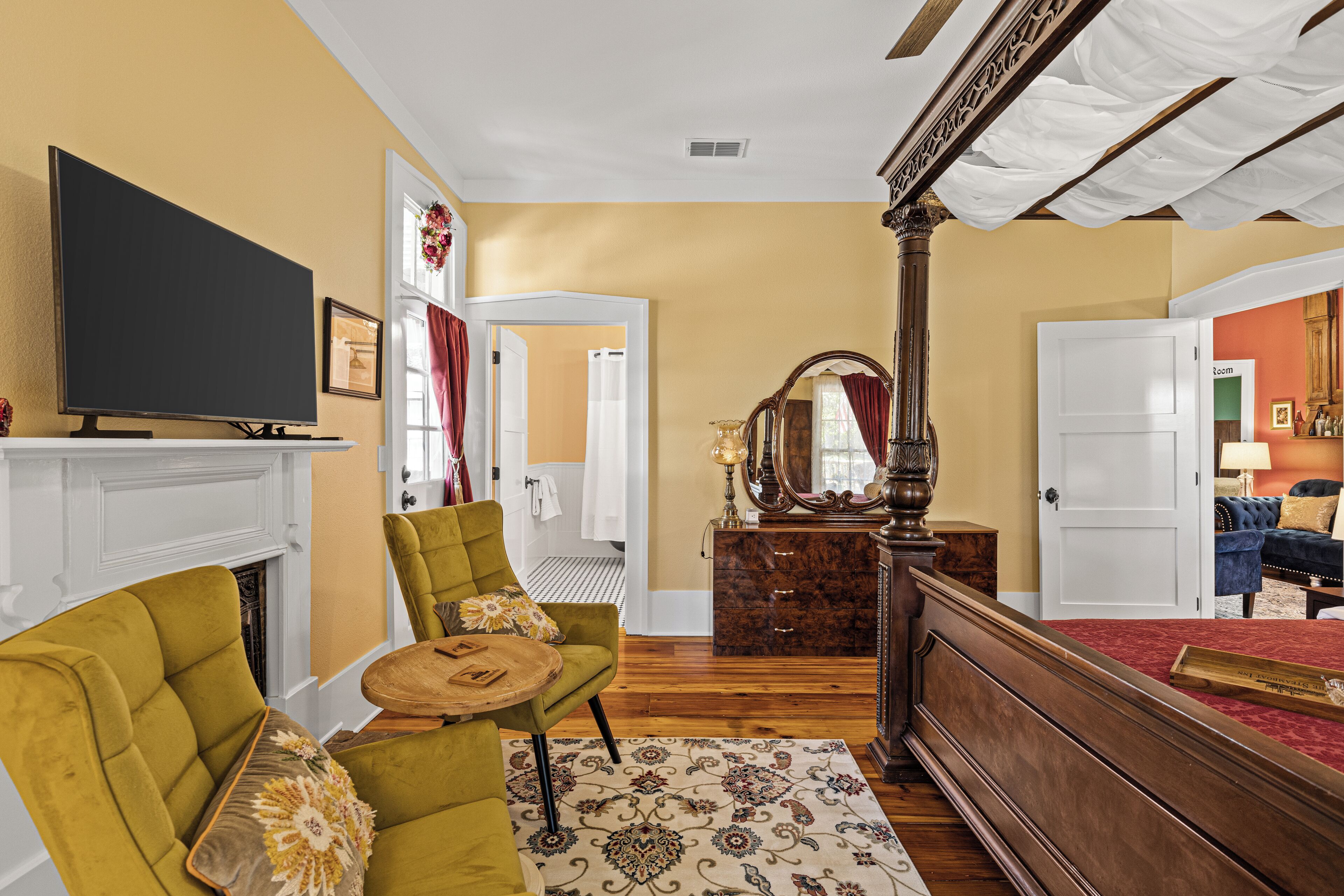 A bedroom with a large bed, a television, a fireplace, and a view into the adjacent bathroom.