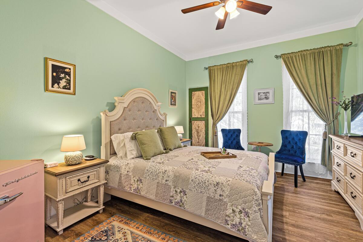 A bedroom with a bed, a dresser, a chair, a nightstand with a lamp, and a ceiling fan.