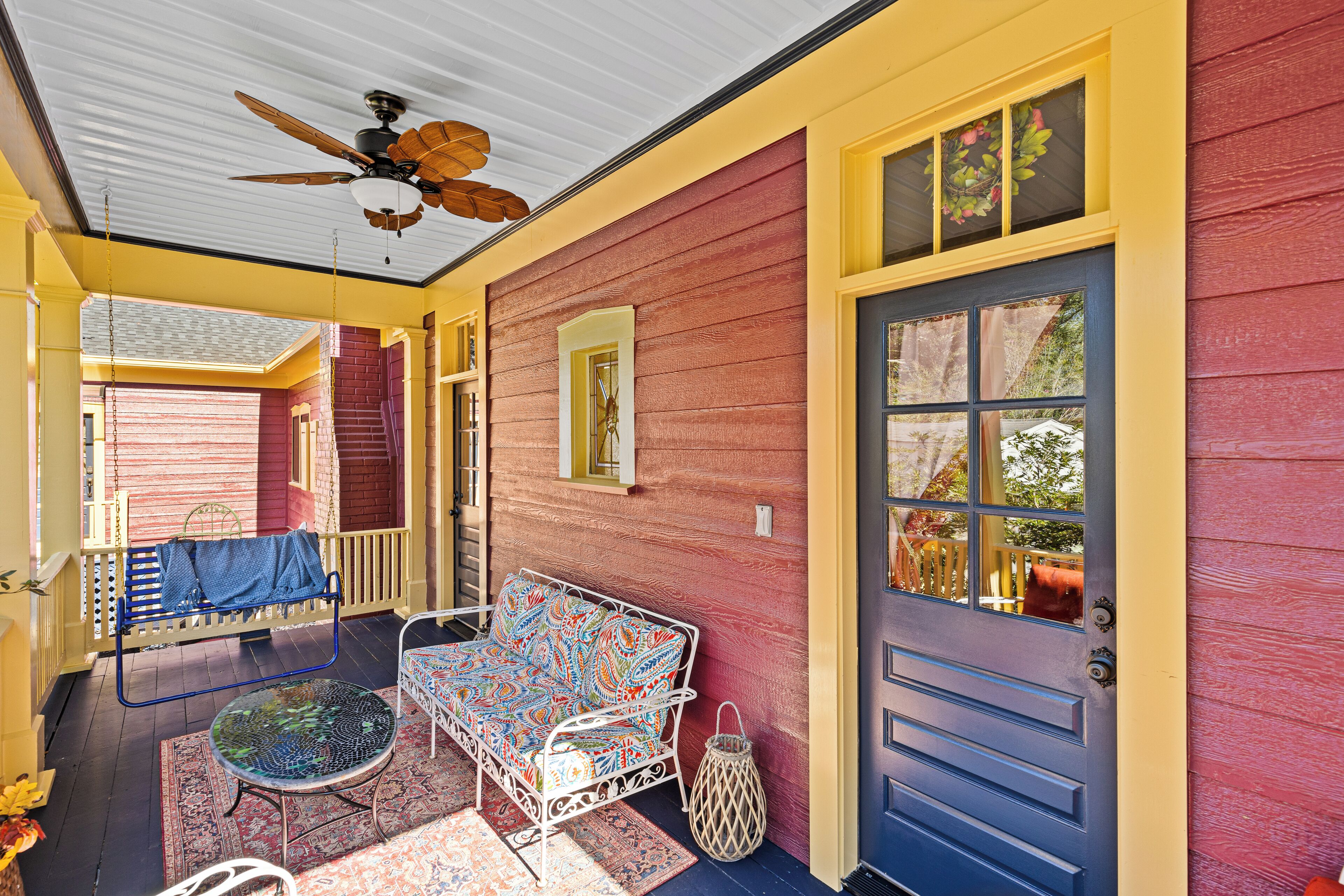 A porch with a blue door, a white bench, and a patterned sofa.