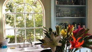 A kitchen with a large window, a vase of flowers, and a bowl of fruit on the counter. - The Steamboat Inn (Jefferson)