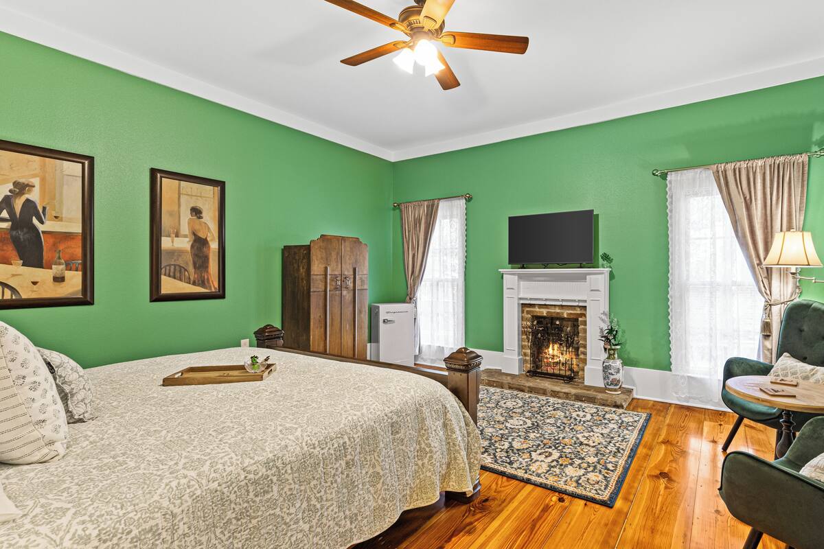 A room with a bed, a fireplace, a television, and green walls.