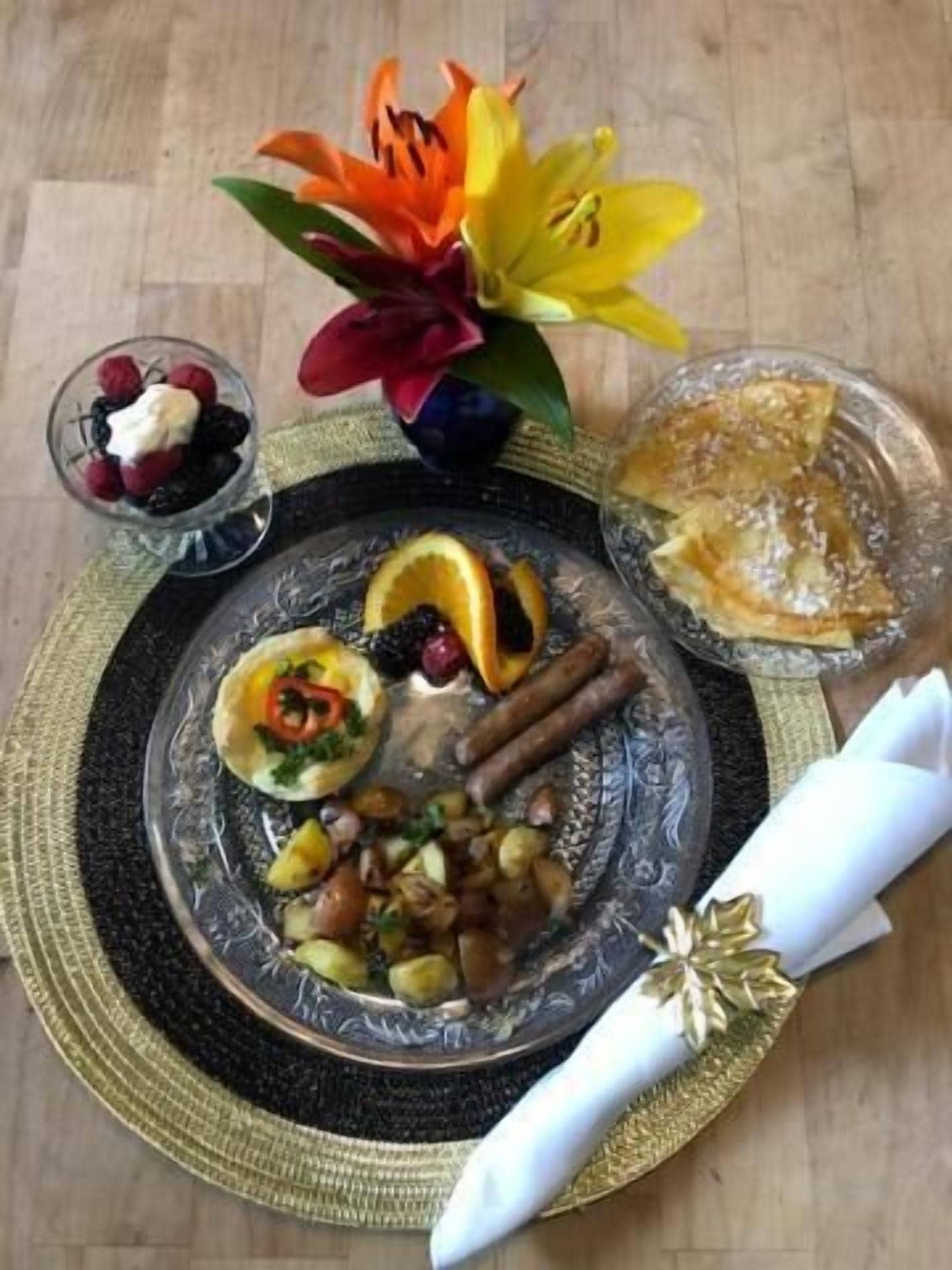 Una mesa de comedor con un plato de comida, un cuenco de fruta y un arreglo floral.