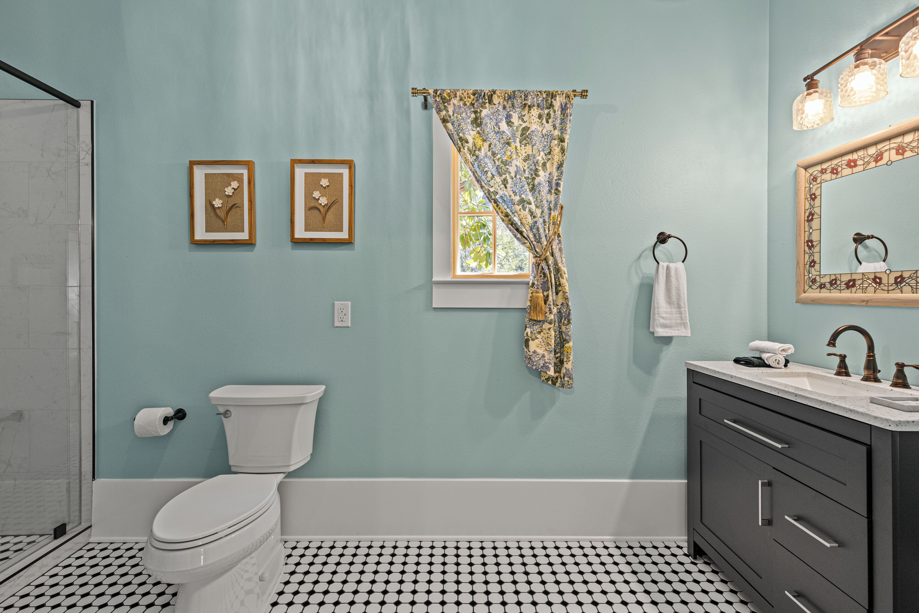 Ein Badezimmer mit Toilette, Waschbecken und Spiegel. An der Wand befinden sich zwei Bilder in Rahmen.
