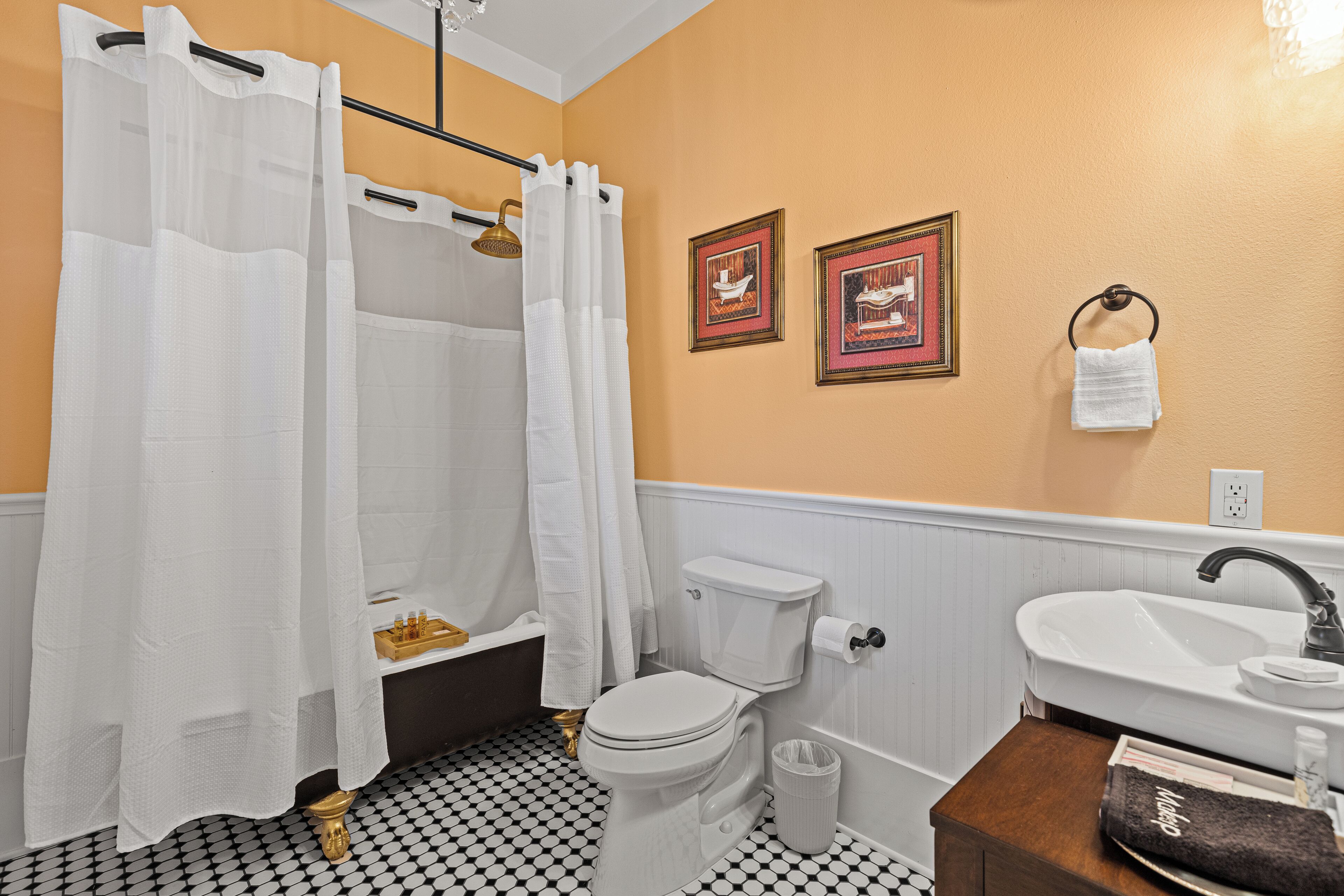 A bathroom with a toilet, sink, and shower curtain. There are two framed pictures on the wall and a towel hanging on a hook.