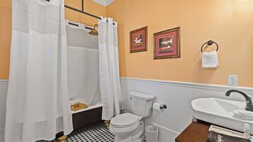 A bathroom with a toilet, sink, and shower curtain. There are two framed pictures on the wall and a towel hanging on a hook.