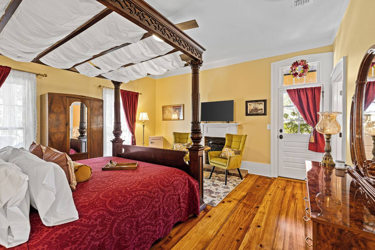 A bedroom with a four-poster bed, a wooden floor, a fireplace, and a television.