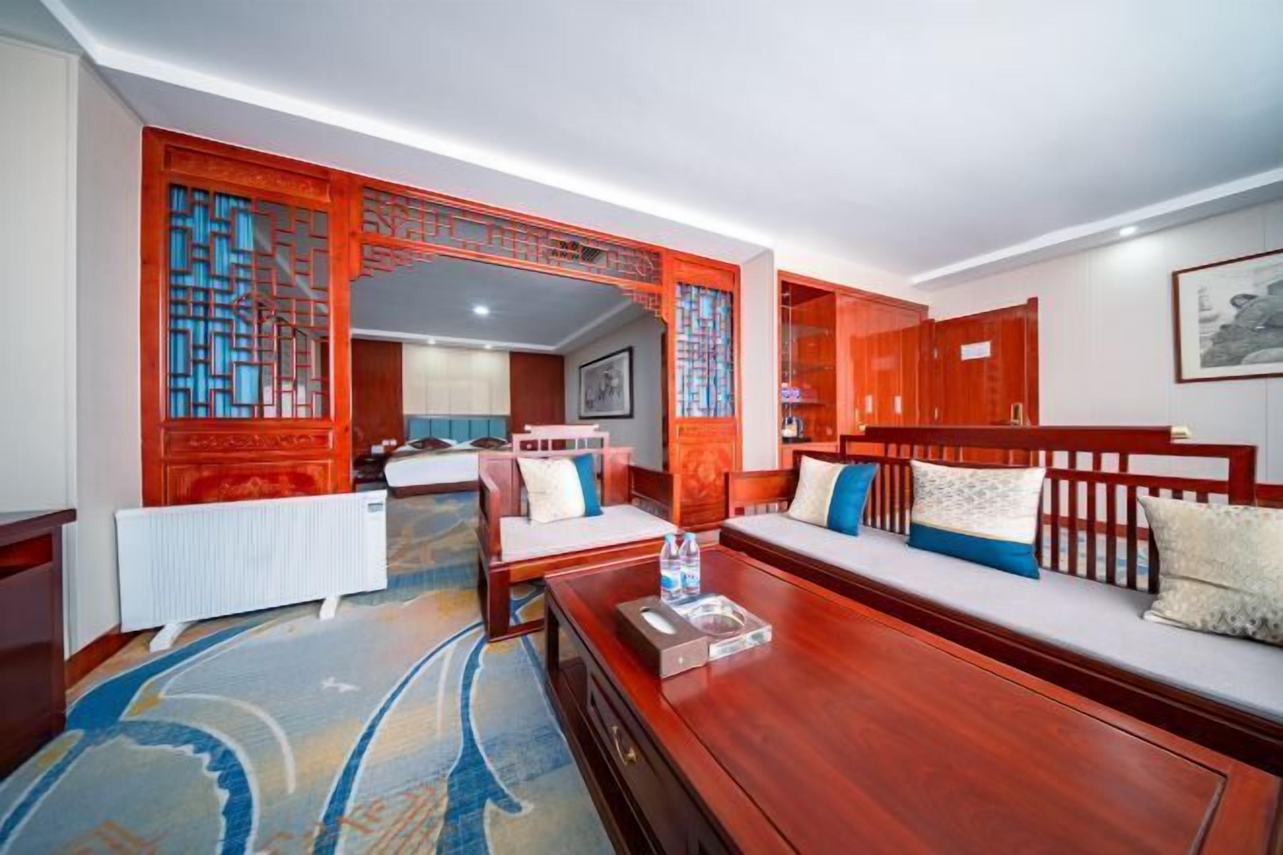 A hotel room with a wooden sofa, a small table with a bottle, a radiator, and a patterned carpet.