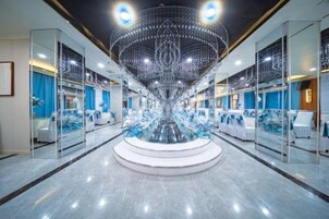 A hotel lobby with a central chandelier, seating areas, and a reflective floor.