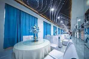 A hotel lobby with round tables, white chairs, and blue curtains.