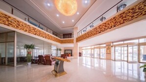 Un hall d’entrée spacieux avec un plafond haut, des motifs d écoratifs sur les murs, un comptoir d’accueil central et de grandes fenêtres laissant entrer la lumière naturelle.