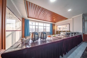 A conference room with a long table, two large pots, and a window with blue curtains.