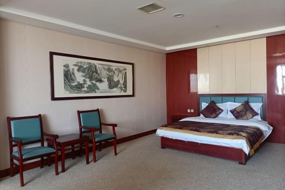 Une chambre d’hôtel avec un lit, deux chaises, un grand tableau encadré et un mur d’accent de couleur rouge.