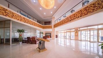 A spacious lobby with a high ceiling, a central art piece, and a staircase leading to an upper level.