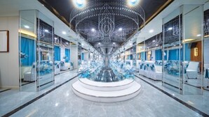 Un hall d’hôtel doté d’un lustre central, de murs recouverts de miroirs et d’espaces aménagés avec des sièges.