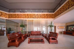 A lobby with a high ceiling, a central seating area with sofas and a coffee table, and a decorative wall pattern.