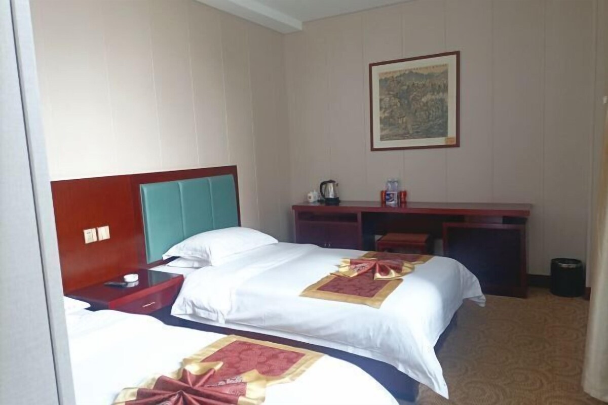 Une chambre d’hôtel avec deux lits, un bureau, une chaise, une machine à café et une poubelle.