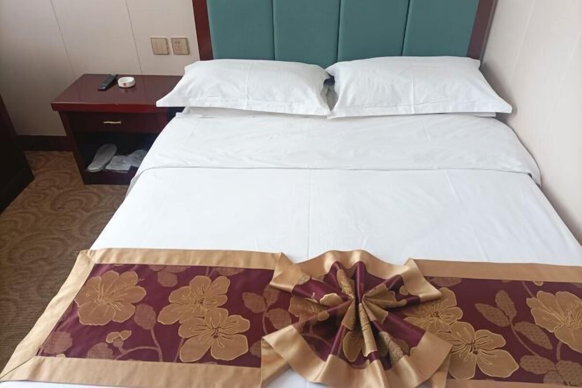 Une chambre d’hôtel avec un lit, une table de chevet et une paire de chaussons posés sur le sol.