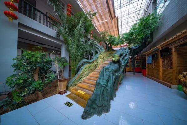 Un atrio de varios niveles con una escalera central, rodeado de plantas de interior y decoración tradicional.