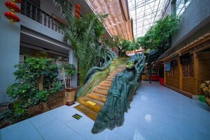 Un atrio de varios niveles con una escalera central, rodeado de plantas de interior y decoración tradicional.