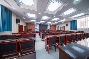 Un salón de conferencias con filas de sillas, un escenario y tragaluces.