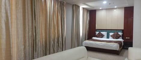 A hotel room with a bed, two white sofas, and a large mirror.