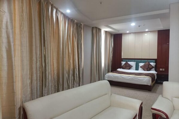 Une chambre d’hôtel avec un lit, deux canapés blancs et un grand miroir.