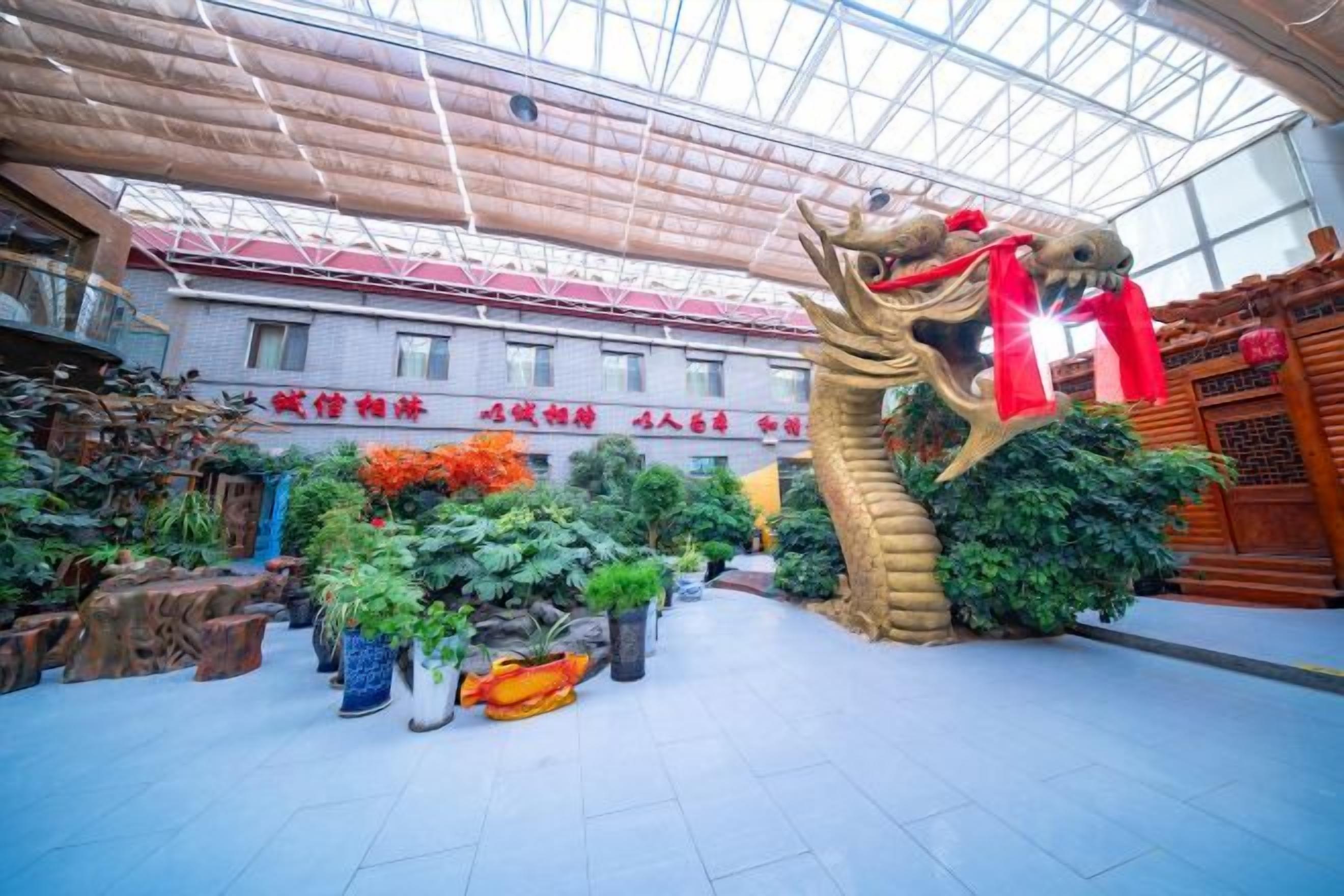 A spacious indoor area with a large dragon sculpture, potted plants, and a building with signage in the background.