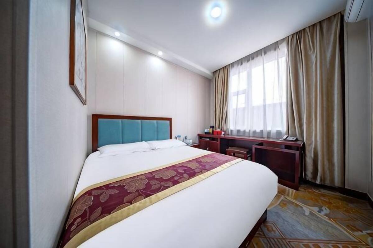 Ein Hotelzimmer mit einem großen Bett, einem Schreibtisch und einem Fenster mit Vorhängen.