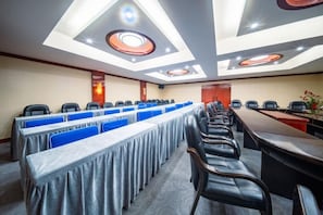 Een vergaderzaal met een lange tafel, rijen stoelen en een plafond met inbouwverlichting.