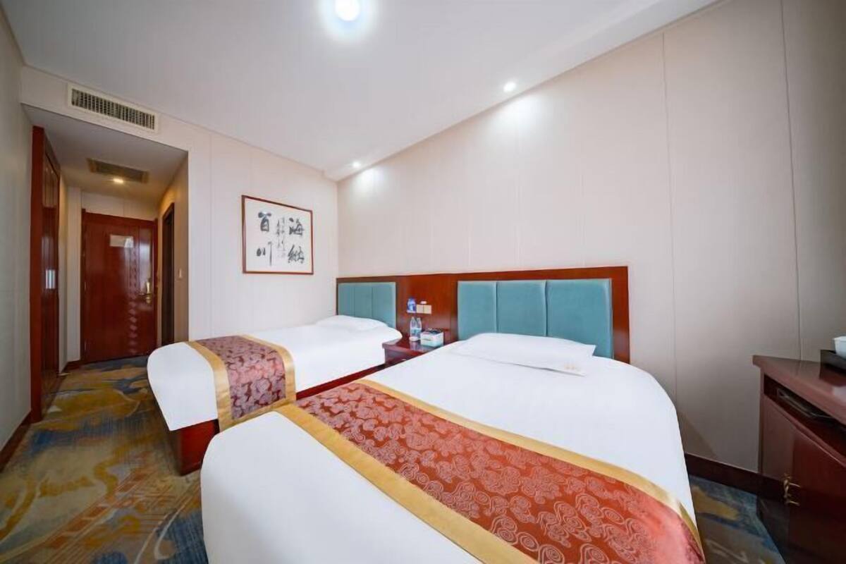 Ein Hotelzimmer mit zwei Betten, einem hölzernen Kopfteil, einem Nachttisch und einem gerahmten Bild an der Wand.