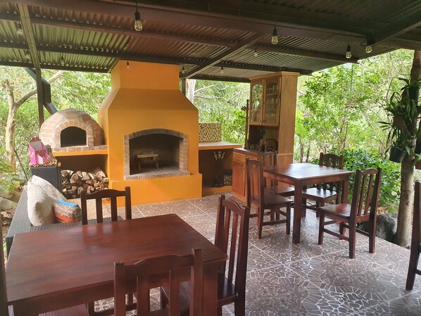Un patio al aire libre con horno de ladrillo, mobiliario de madera y suelo de baldosas.