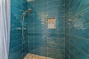 Ein Badezimmer mit blauen Fliesen, einer Dusche und einem Ablagefach mit Pflegeprodukten.