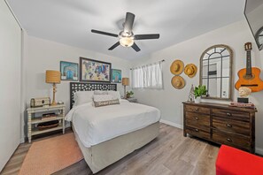 A bedroom with a bed, a dresser, a ceiling fan, a guitar, and decorative items.