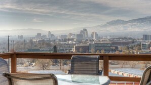 Stadsbeeld met bergen op de achtergrond, zichtbaar vanaf een balkon met stoelen en een tafel.