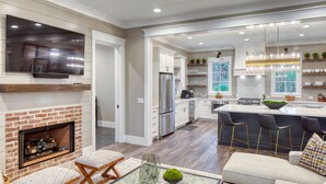 A modern kitchen with a central island, built-in appliances, and a dining area with bar stools. - Lake Views  + Porch Movies, Game Nights and Hot Tub (Bluffton)