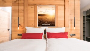 Un dormitorio con cabecera de madera, dos camas blancas con almohadas rojas, un cartel en la pared y un armario de madera.