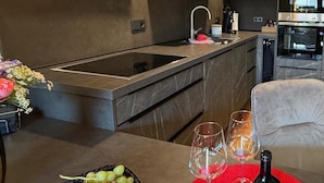 Una cocina moderna con horno empotrado, un lavamanos y un comedor con mantel rojo, copas de vino y una botella.