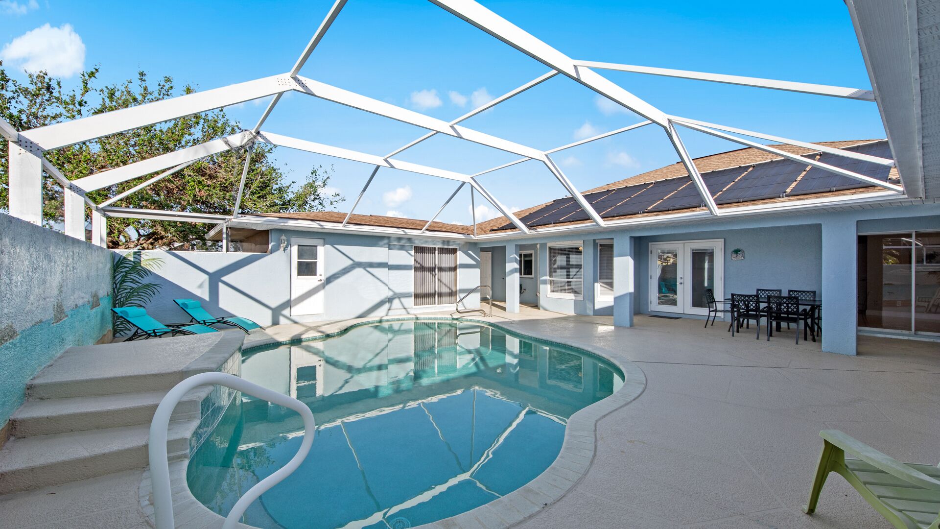 A swimming pool with a glass enclosure, a patio area with outdoor furniture, and a house with a tiled roof.