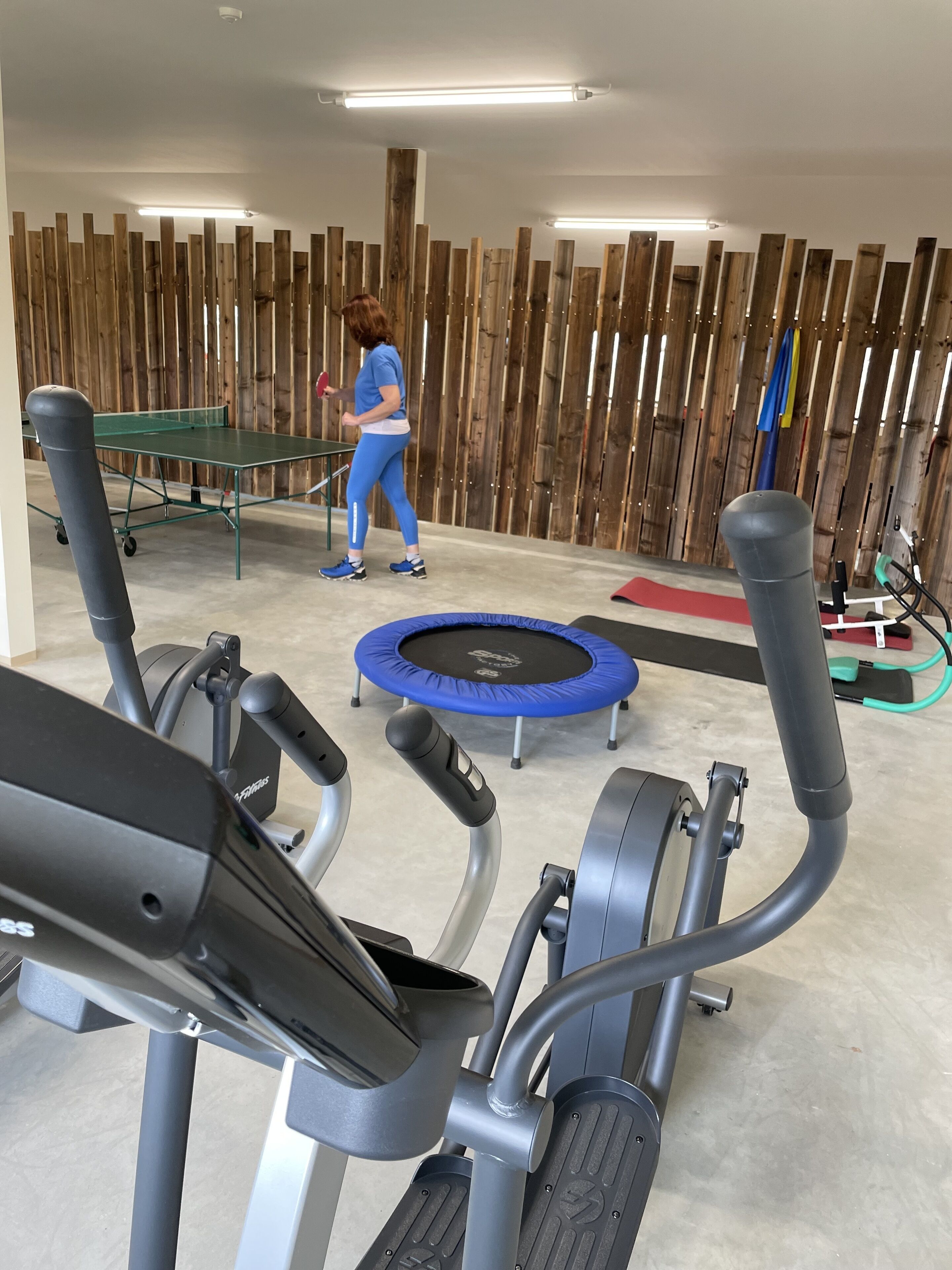 A gym with exercise equipment including treadmills, a trampoline, and a wooden wall in the background.