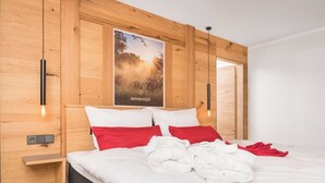 A modern hotel room with a wooden headboard, a large poster of a natural landscape, and a neatly made bed with red and white bedding.