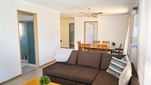 Sala de estar com sofá marrom, mesa de centro de madeira com uma planta, ventilador de teto e área de jantar ao fundo.