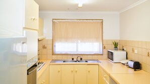 Cozinha com pia, fogão, micro-ondas e uma janela com cortinas.