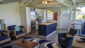 A modern kitchen with a central island, a dining area with a wooden table, and a living room with a sofa and chairs.
