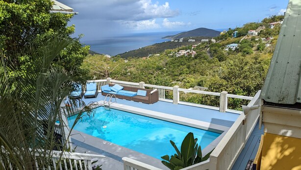 A rectangular pool with a white deck and blue lounge chairs, surrounded by white railings and potted plants.