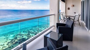 A balcony with a glass railing overlooking turquoise ocean waters and coral reefs. There are wicker chairs and a small table. - Ocean paradise - Relax & refresh - Villa Paradiso (San Miguel de Cozumel)