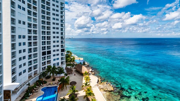 A resort with a large pool, palm trees, and a view of the ocean. - Ocean paradise - Relax & refresh - Villa Paradiso (San Miguel de Cozumel)