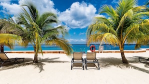 A beach with two lounge chairs, palm trees, and a lifebuoy. - Ocean paradise - Relax & refresh - Villa Paradiso (San Miguel de Cozumel)